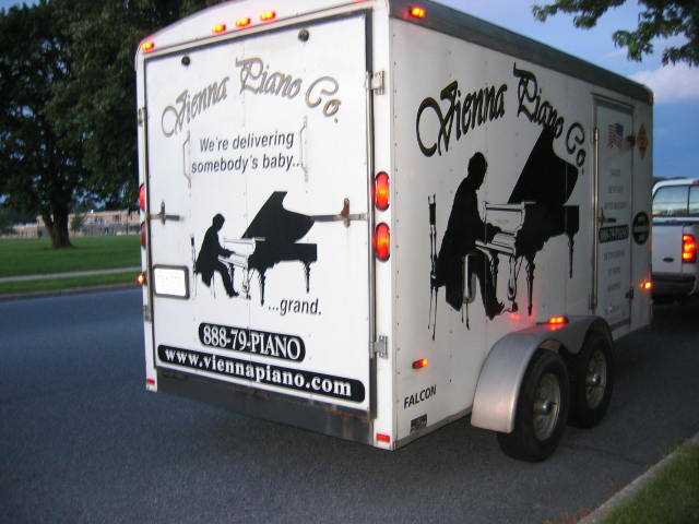 Small white enclosed trailer with silhouette of a man playing a baby grand piano